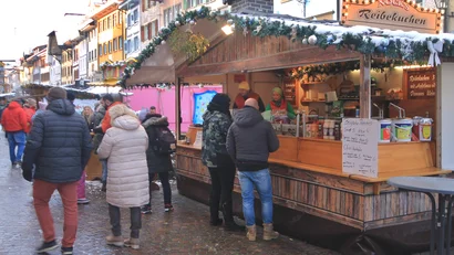 Menschen vor einem Holzstand mit winterlicher Dekoration auf einem Weihnachtsmarkt