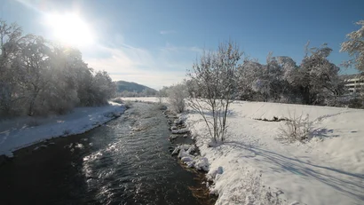 Fluss im Winter mit schneebedeckten Bäumen und klar blauem Himmel