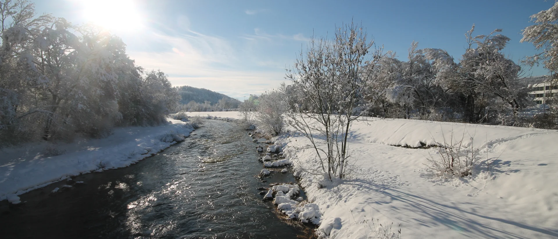 Das 4-Sterne-Hotel Bercher Fluss im Winter mit schneebedeckten Bäumen und klar blauem Himmel
