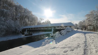 Überdachte Holzbrücke über einen Fluss im verschneiten Winterlandschaft