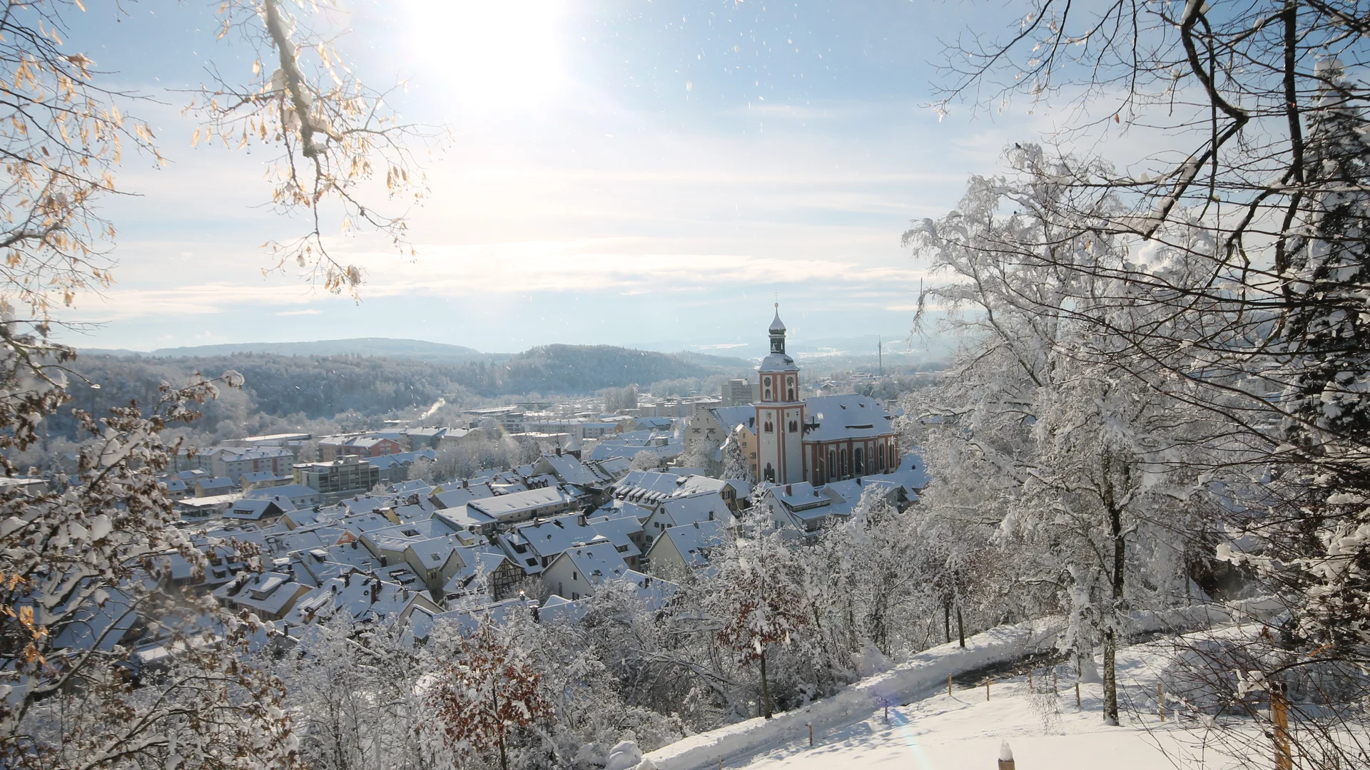Winterlicher Blick auf verschneite Stadt mit Kirche und Bäumen bei Sonnenschein