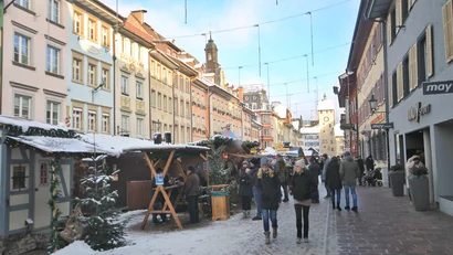 Winterliche Einkaufsstraße mit Schnee, Ständen und Menschen in einer historischen Stadt
